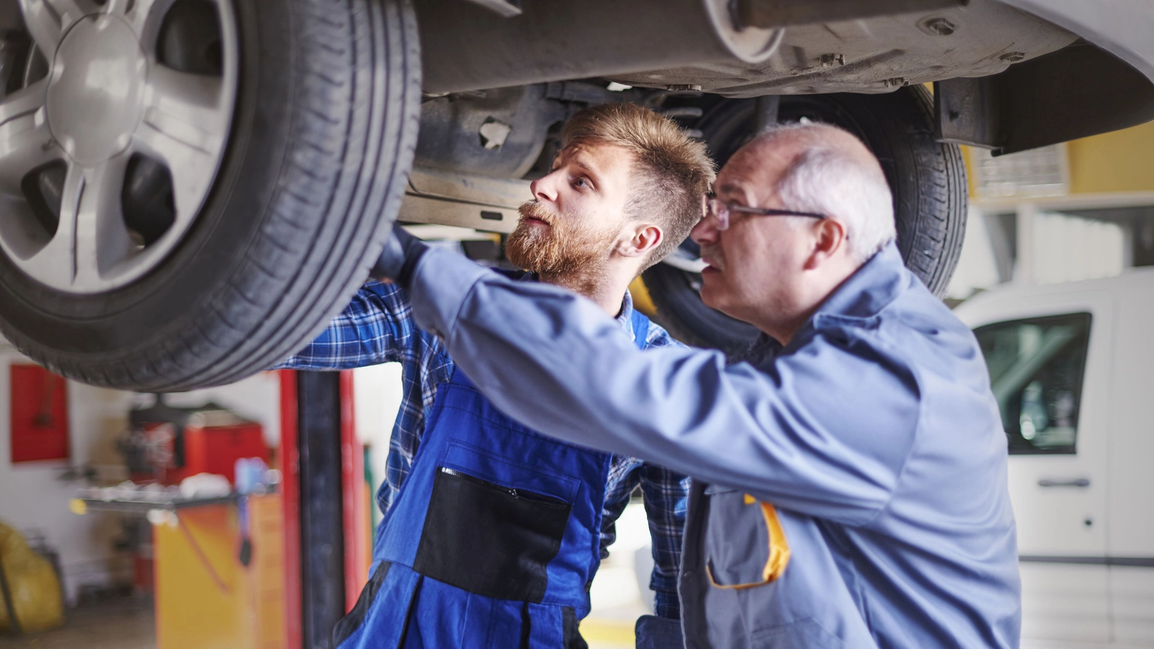 Zwei Kfz-Mechaniker prüfen den Unterboden eines Autos