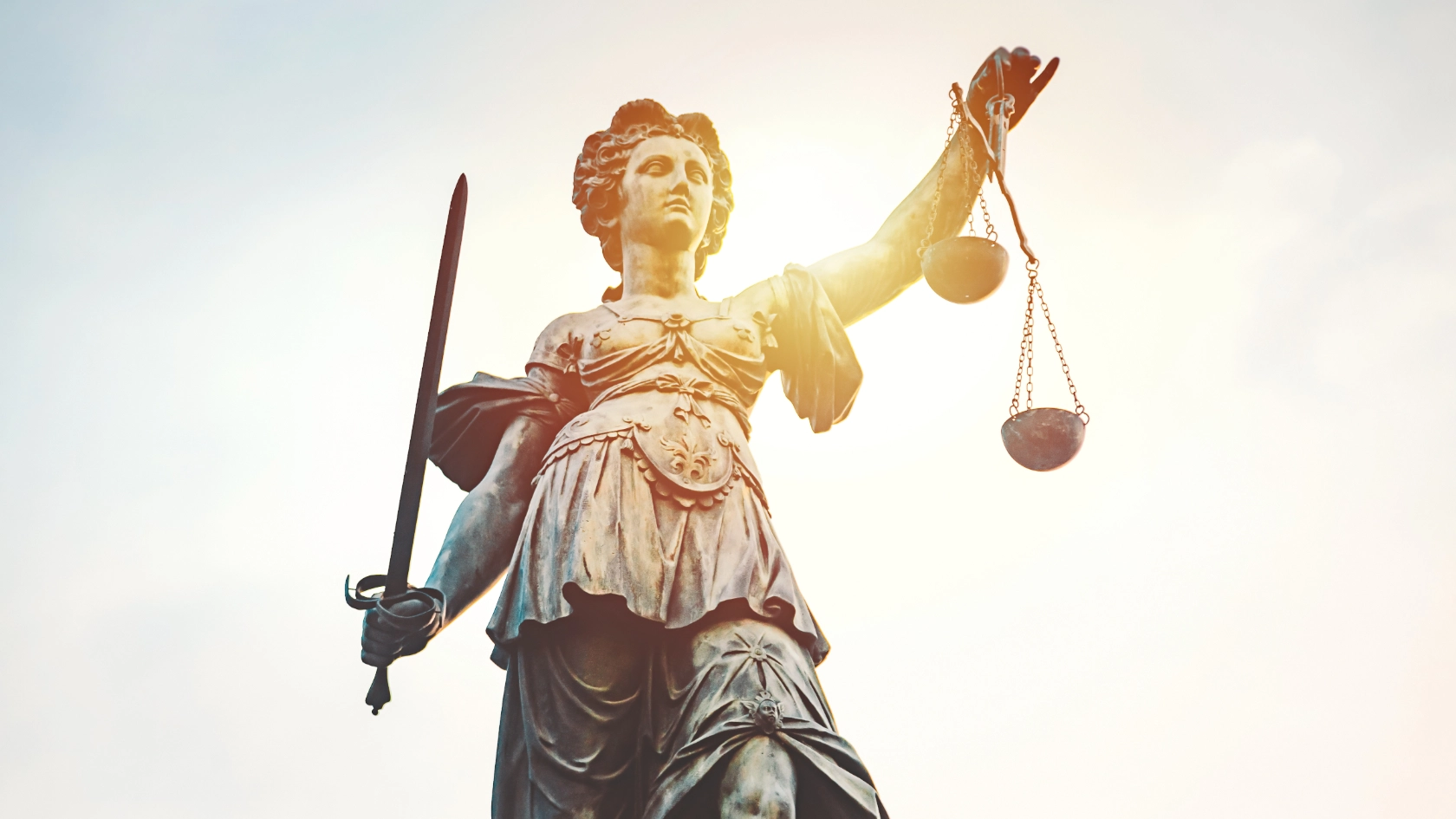 Statue von Justizia mit Schwert und Waage in der Hand vor blauem Himmel