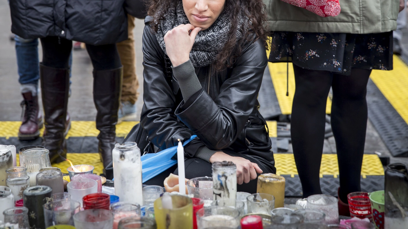 Teilnehmerin einer Trauerfeier kniet vor Kerzen und hält inne