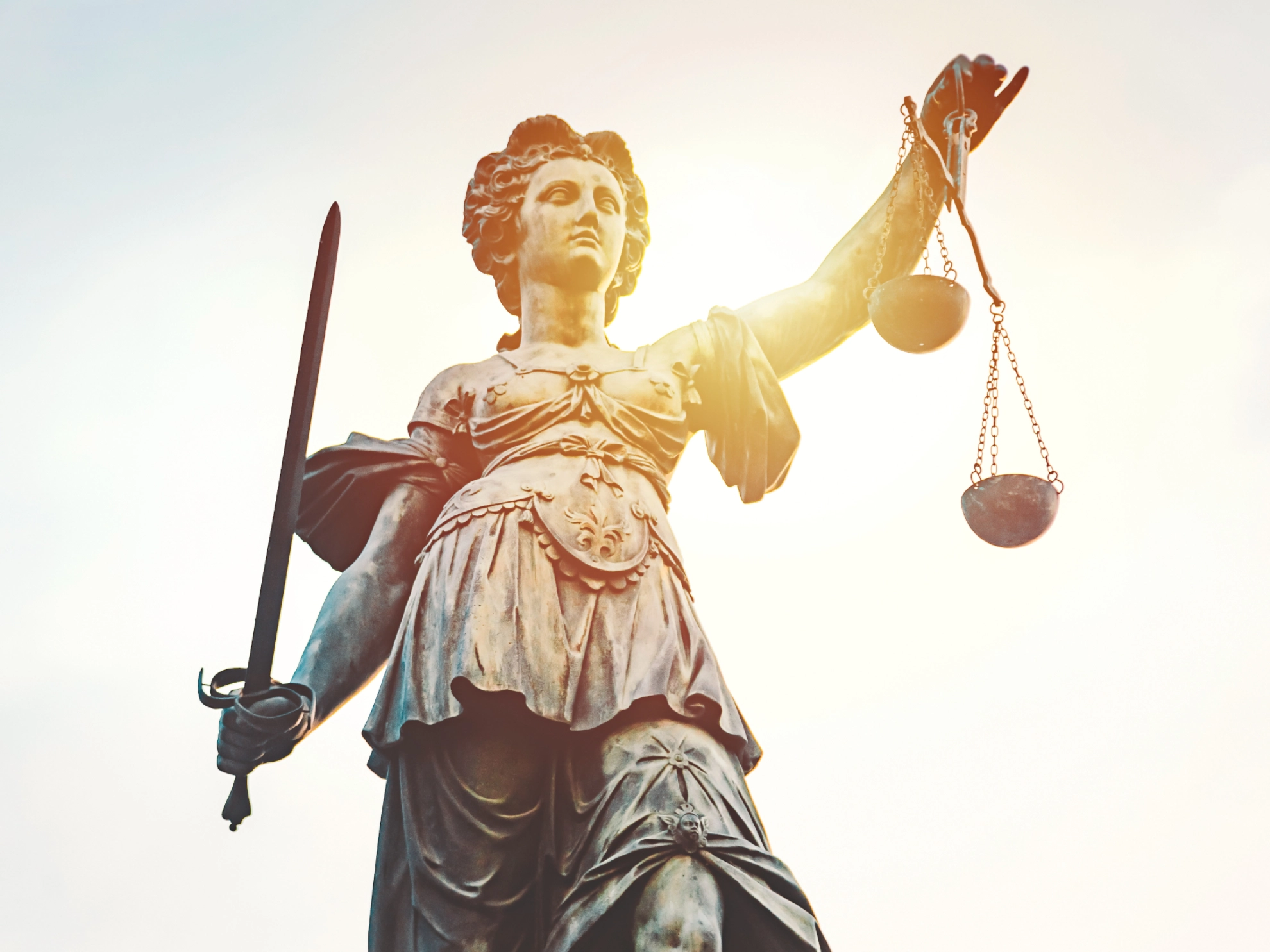 Statue von Justizia mit Schwert und Waage in der Hand vor blauem Himmel
