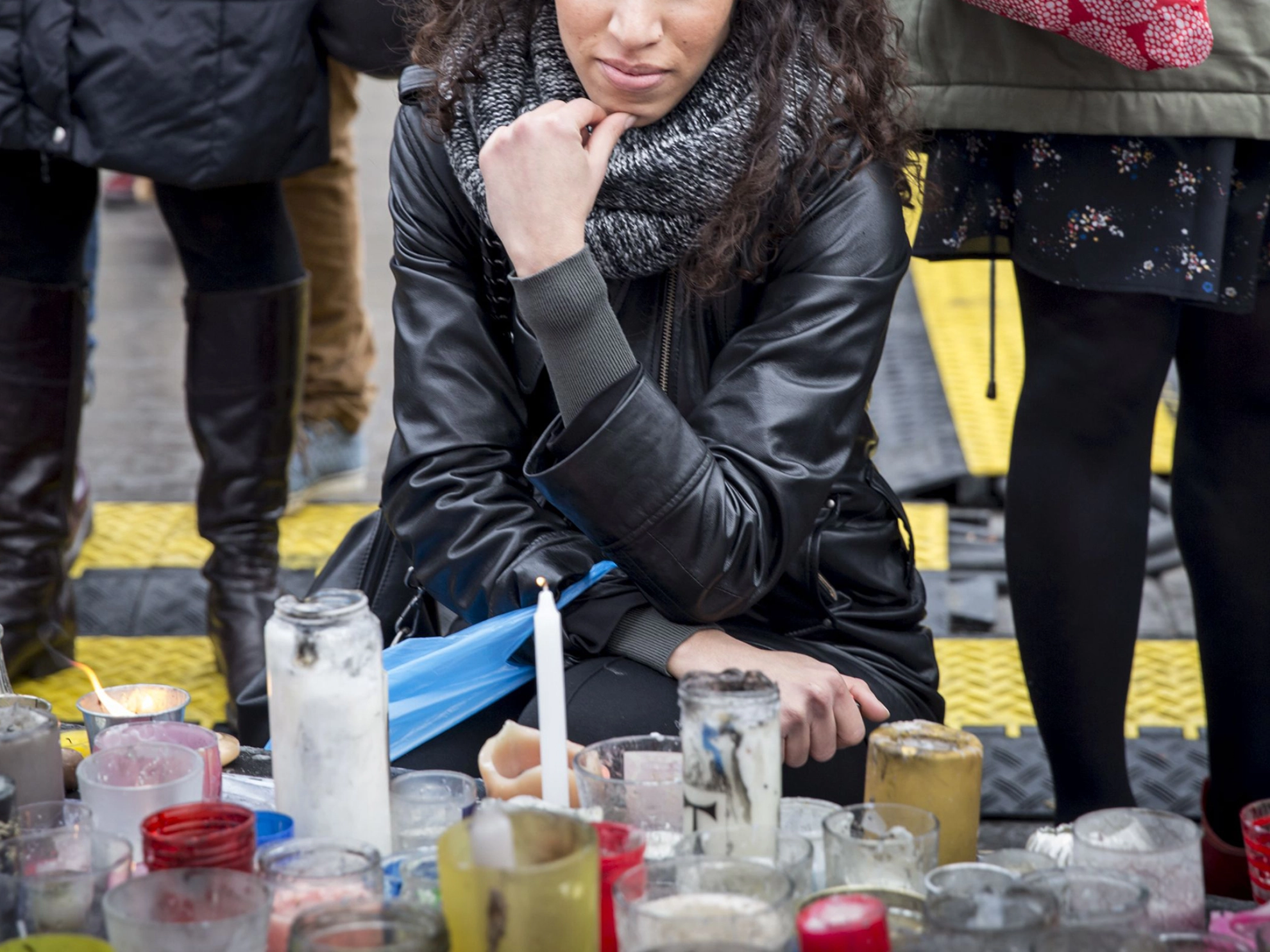 Teilnehmerin einer Trauerfeier kniet vor Kerzen und hält inne